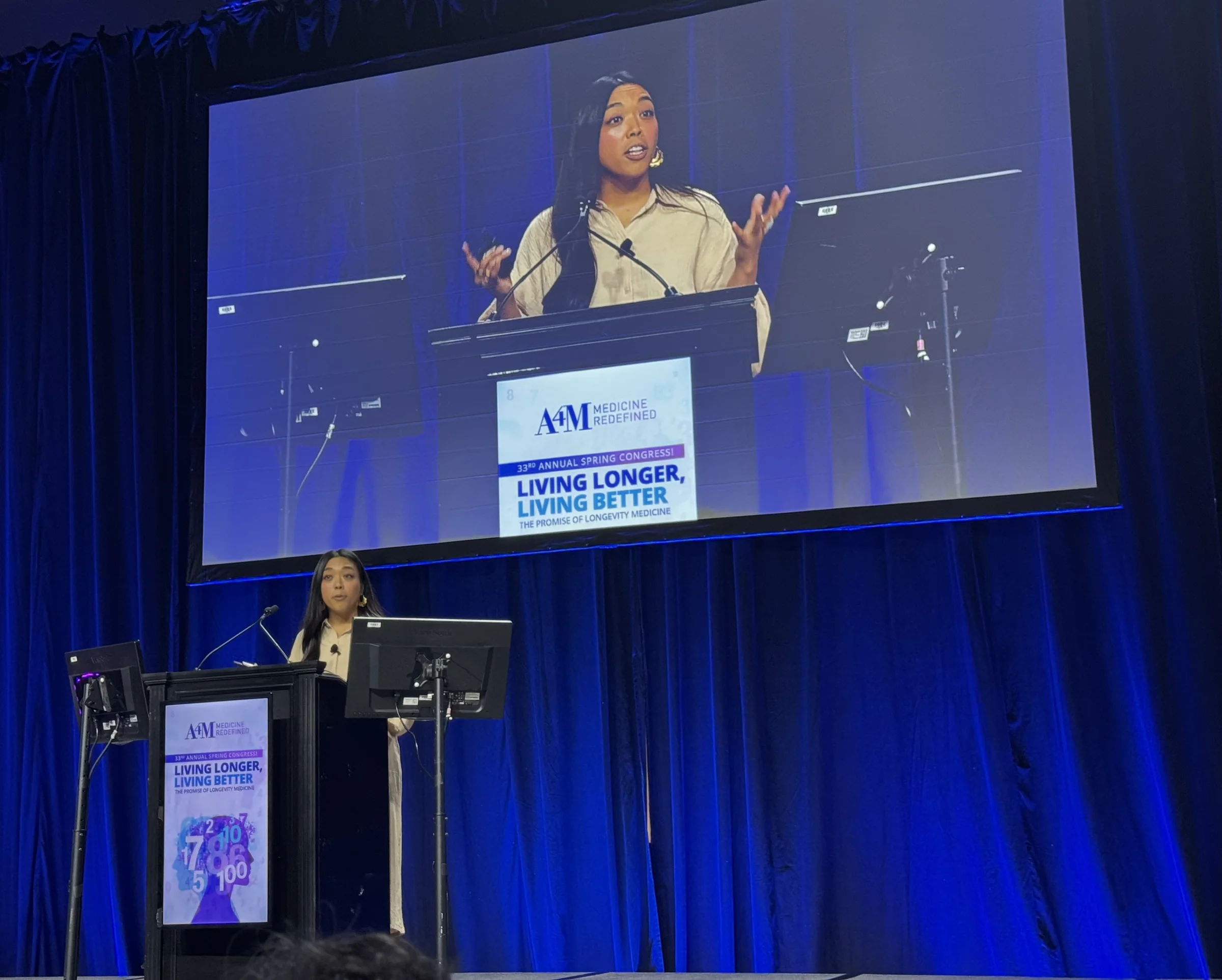 Dr. Lexi Gonzales on the A4M Spring Congress main stage, with the big screen behind her